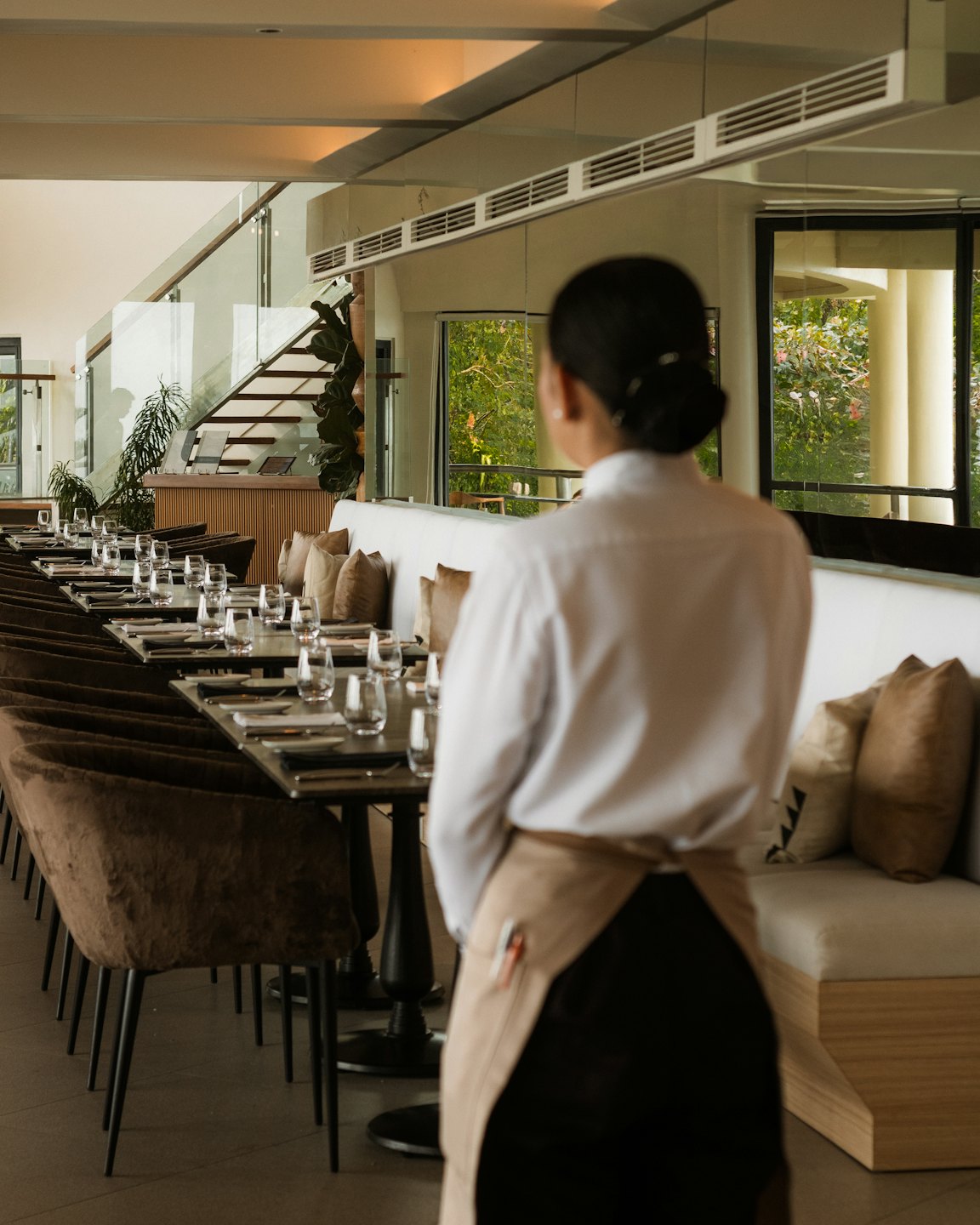 Un camarero con delantal observa el comedor de un restaurante moderno.