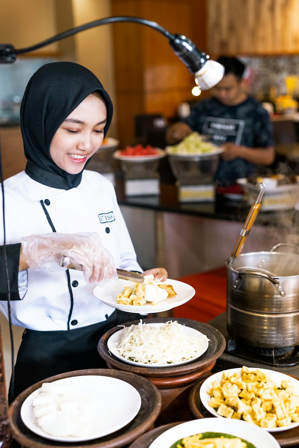 Chef con hiyab sirve comida en una línea de buffet.